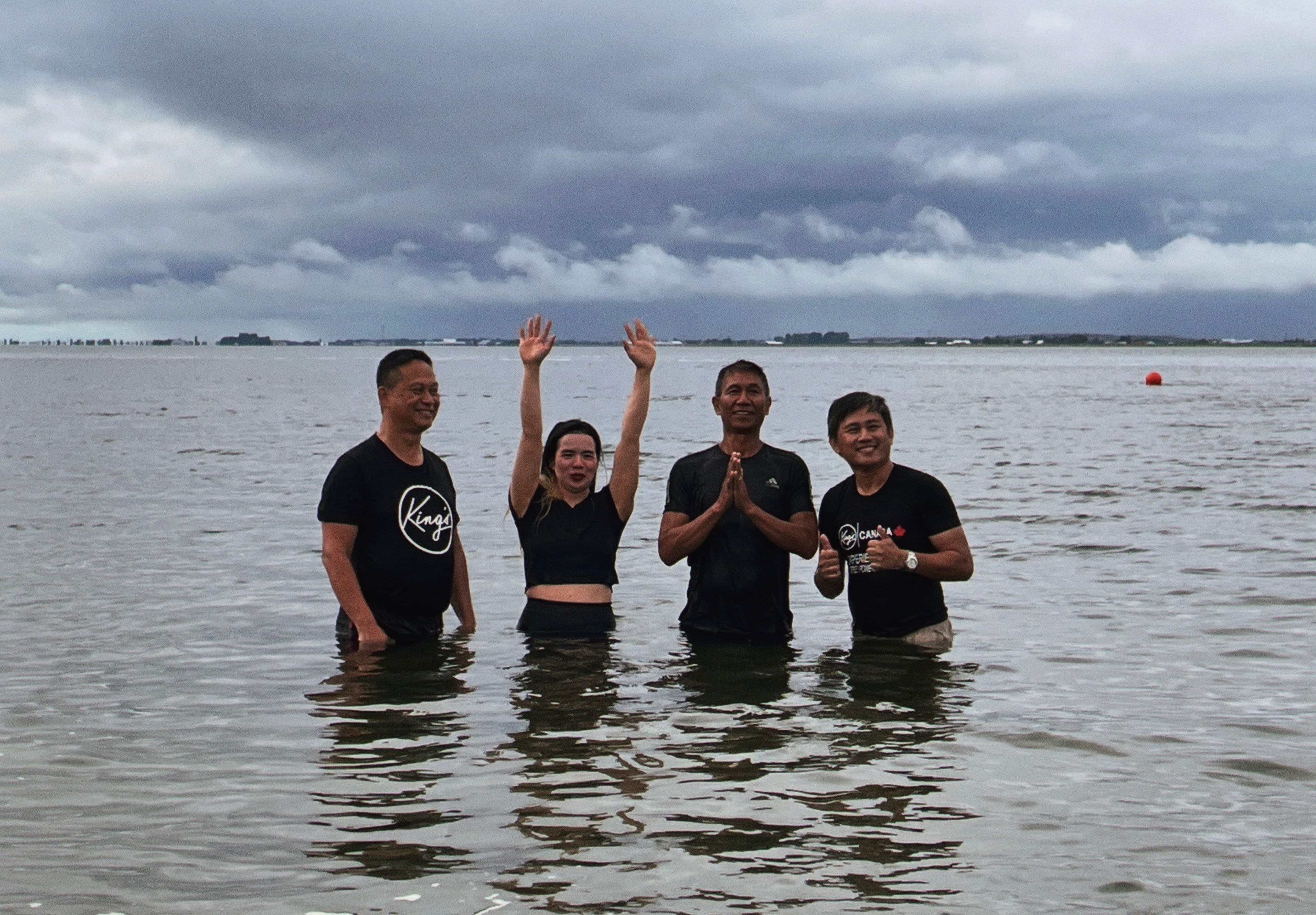 Four people standing together in the water, one with raised hands